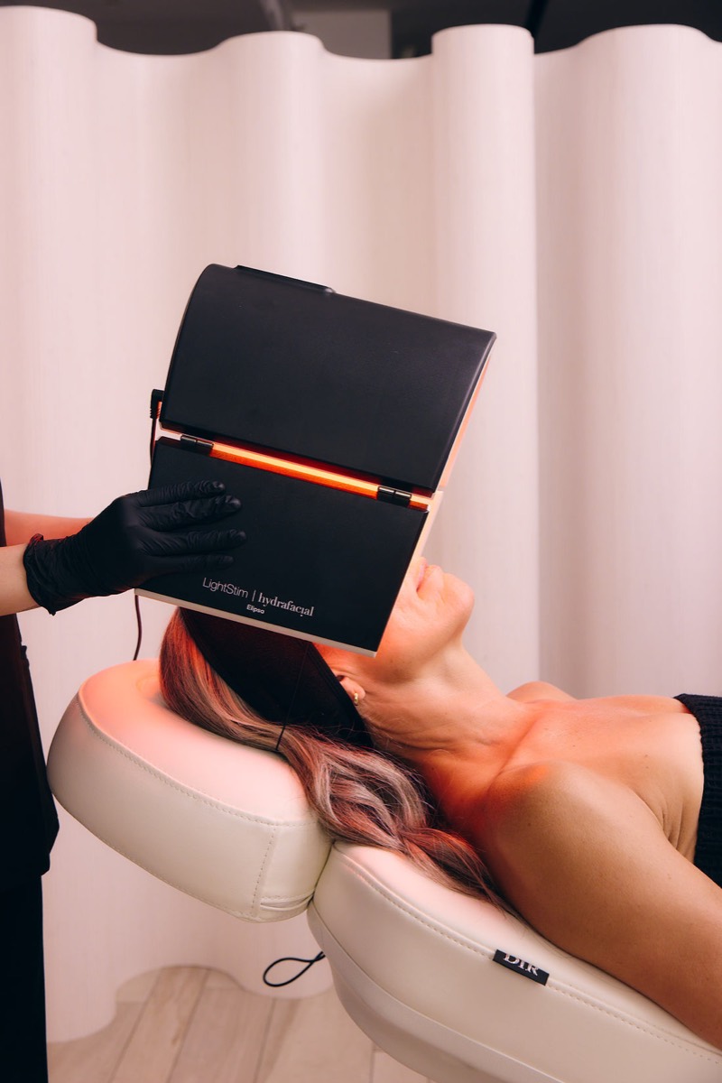 A client relaxes under a Hydrafacial LED light panel during the finishing step